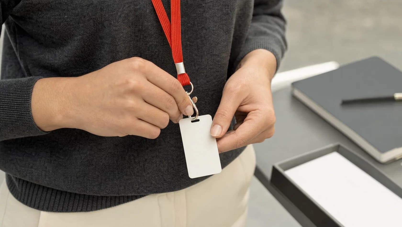 Close up: a hand clipping a plain unmarked card to a lanyard at chest height, no face, flat office daylight.