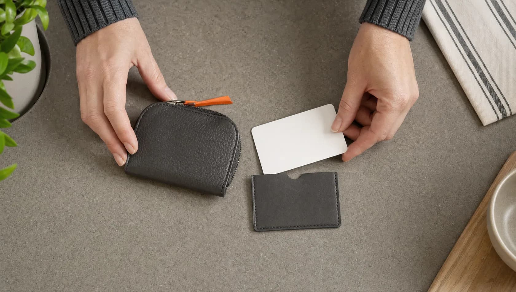 Seen from above: hands laying out a coin purse, a plain card sleeve and a blank card on a kitchen worktop.