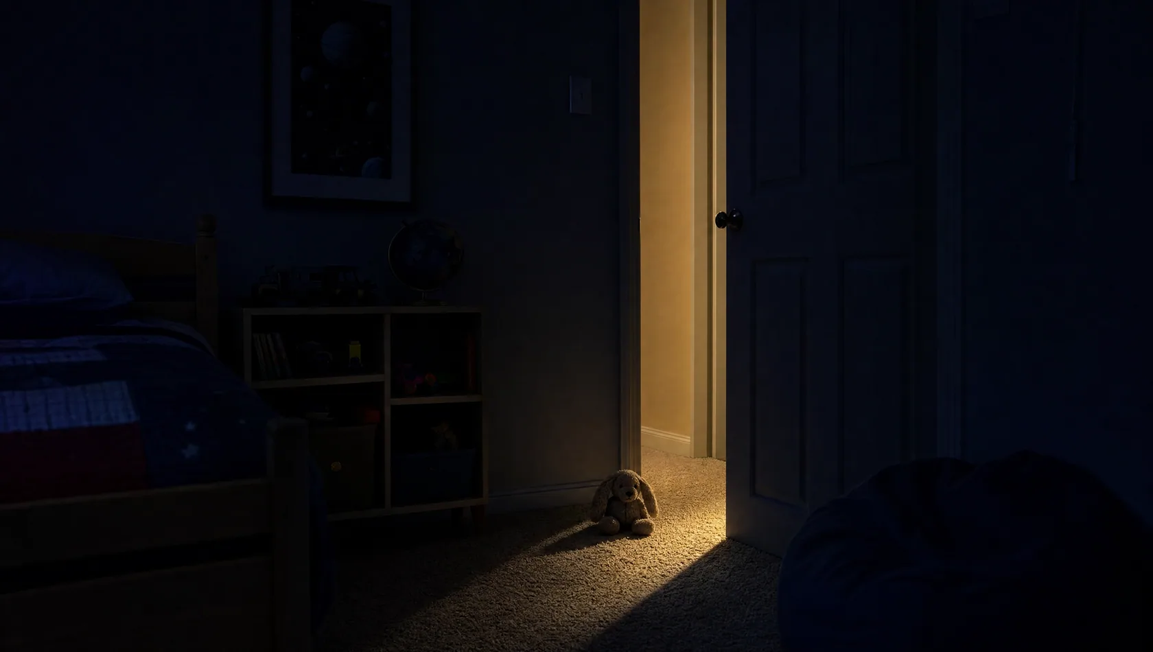 A child's bedroom door ajar at night with a soft band of hall light across the carpet and one toy left just inside, no people.