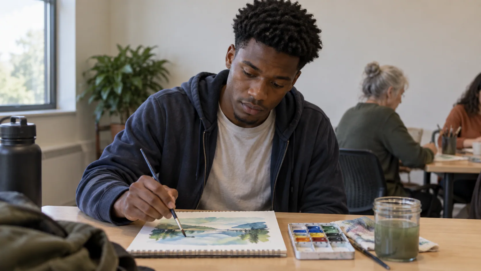 A young Black man trying borrowed watercolor supplies at a community art table.