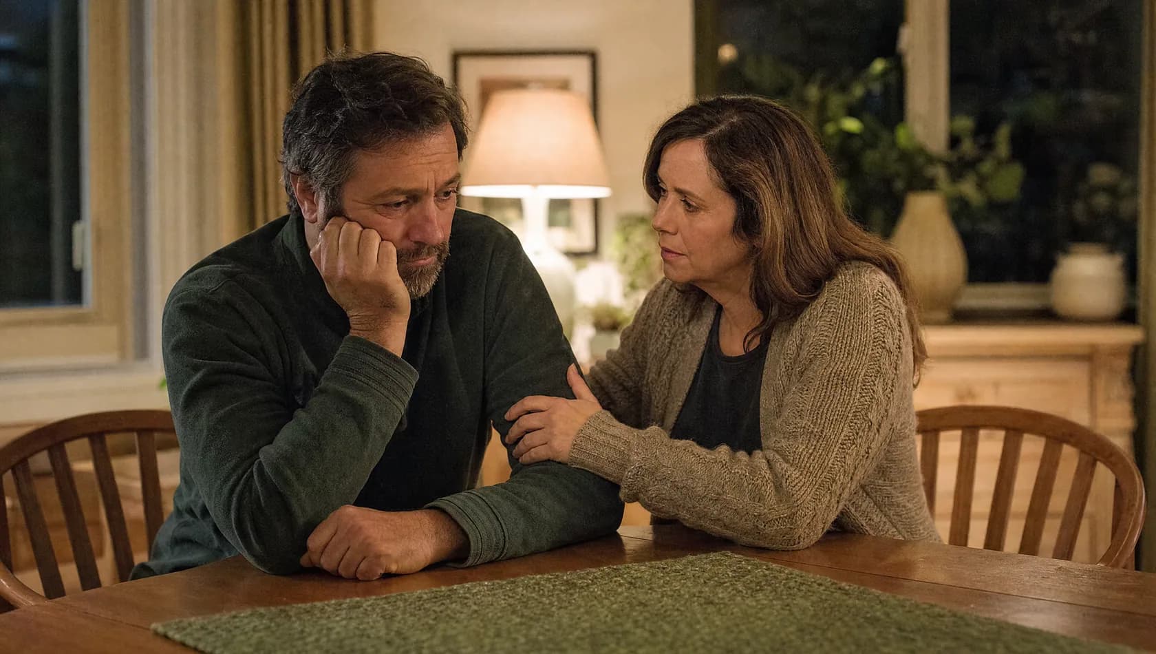 Two worried parents talking at a dining table in the evening.