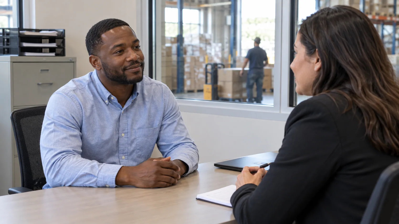 A job applicant and interviewer talking in a warehouse office.