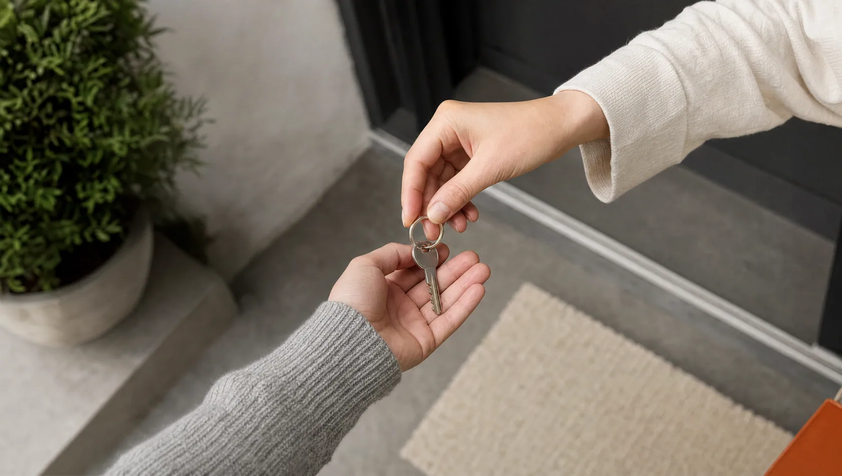 Close up: two hands passing a house key between them above a doorstep, no faces, flat daylight.