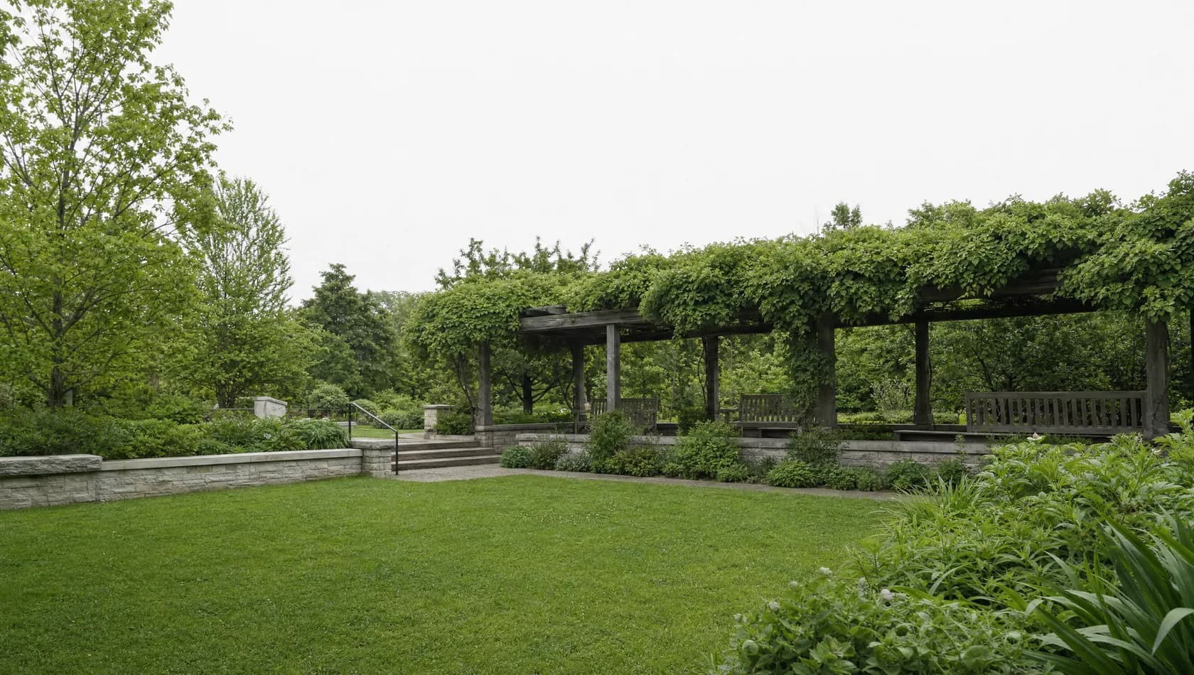 A reading garden behind a public building: low walls, planted beds and wooden benches under a pergola, no people.