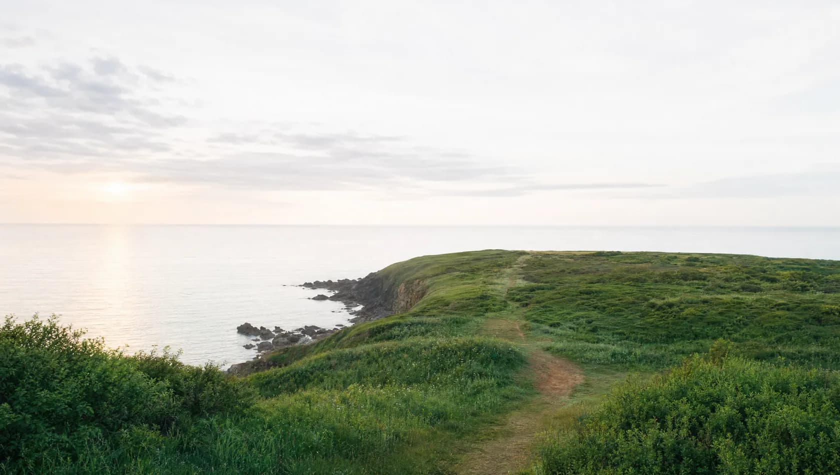 A coastal headland at dawn with a level horizon and a clear path along the cliff top, no people.